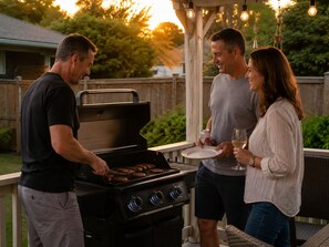 A barbecue grill with sausages being cooked, a wooden deck, and a covered seating area with hanging lights. - Relaxing Pool Retreat Near Wineries & Point Pelee (Kingsville)