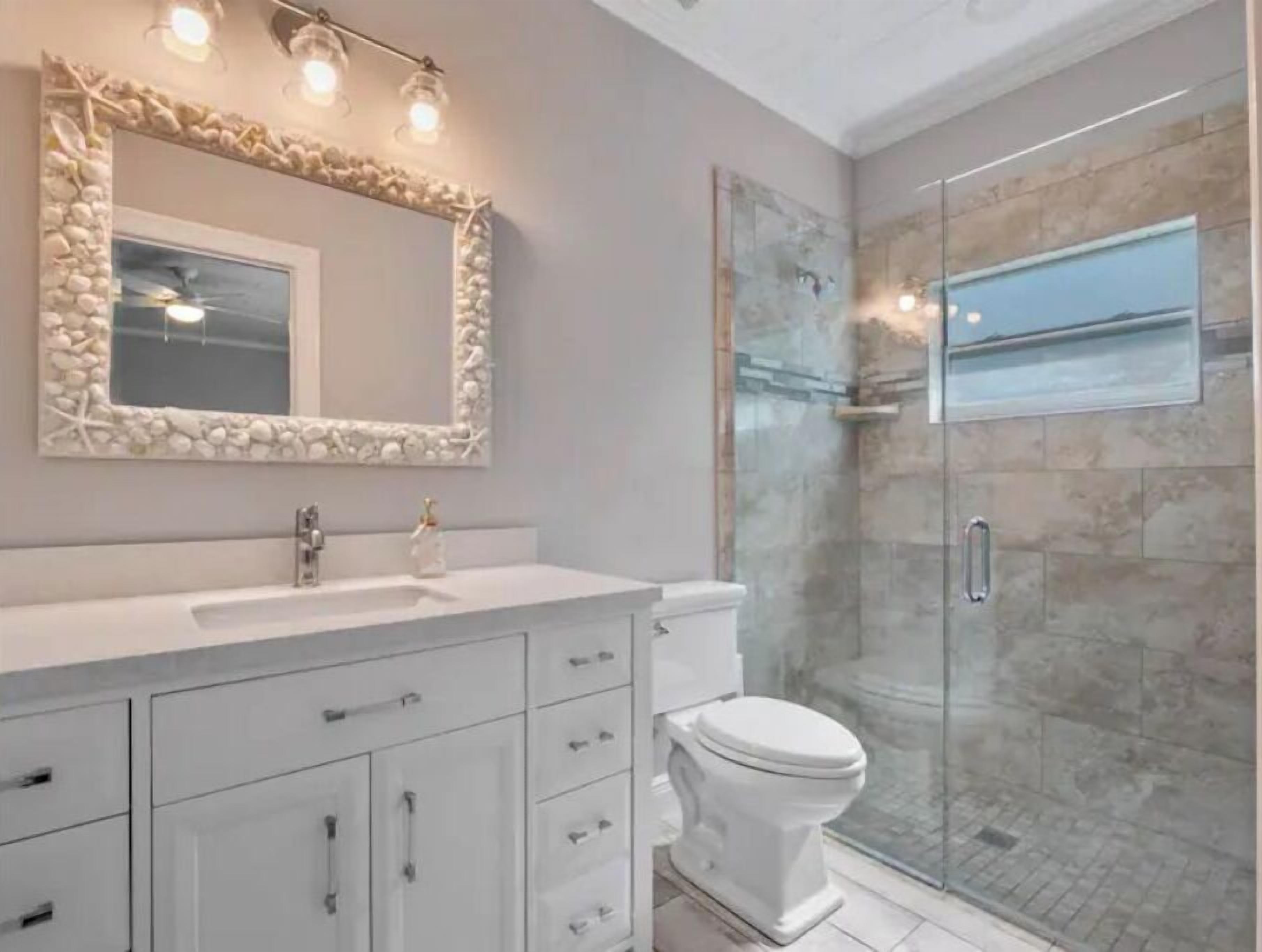 Une salle de bain avec un meuble-lavabo blanc, un grand miroir avec un cadre décoratif, des toilettes et une douche à parois de verre.