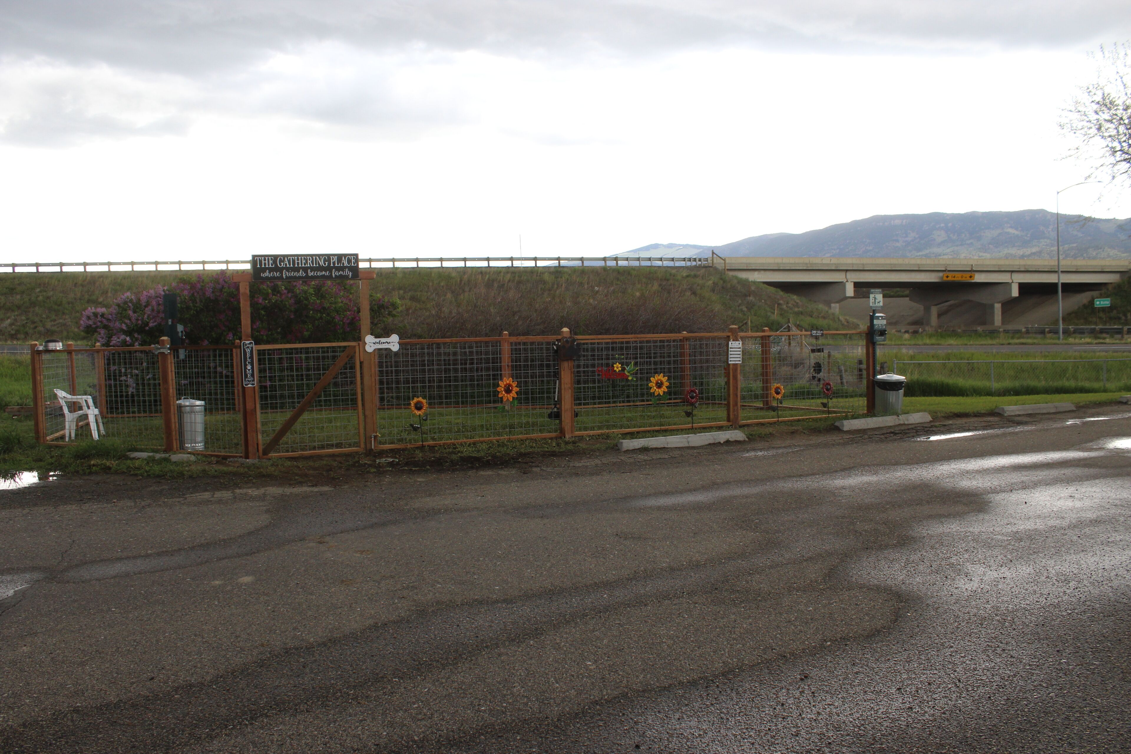A gated entrance with a sign reading "The Gathering Place" and a view of a bridge and mountains in the background.