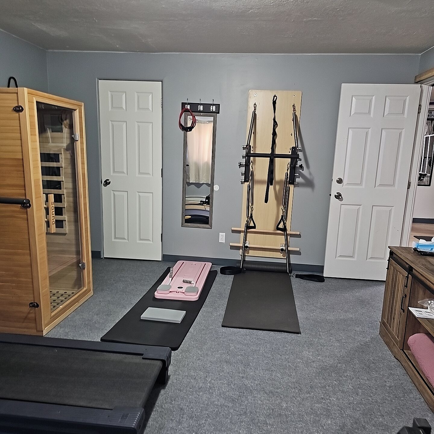 A room with a wooden door, a mirror, a pull-up bar, and exercise mats.