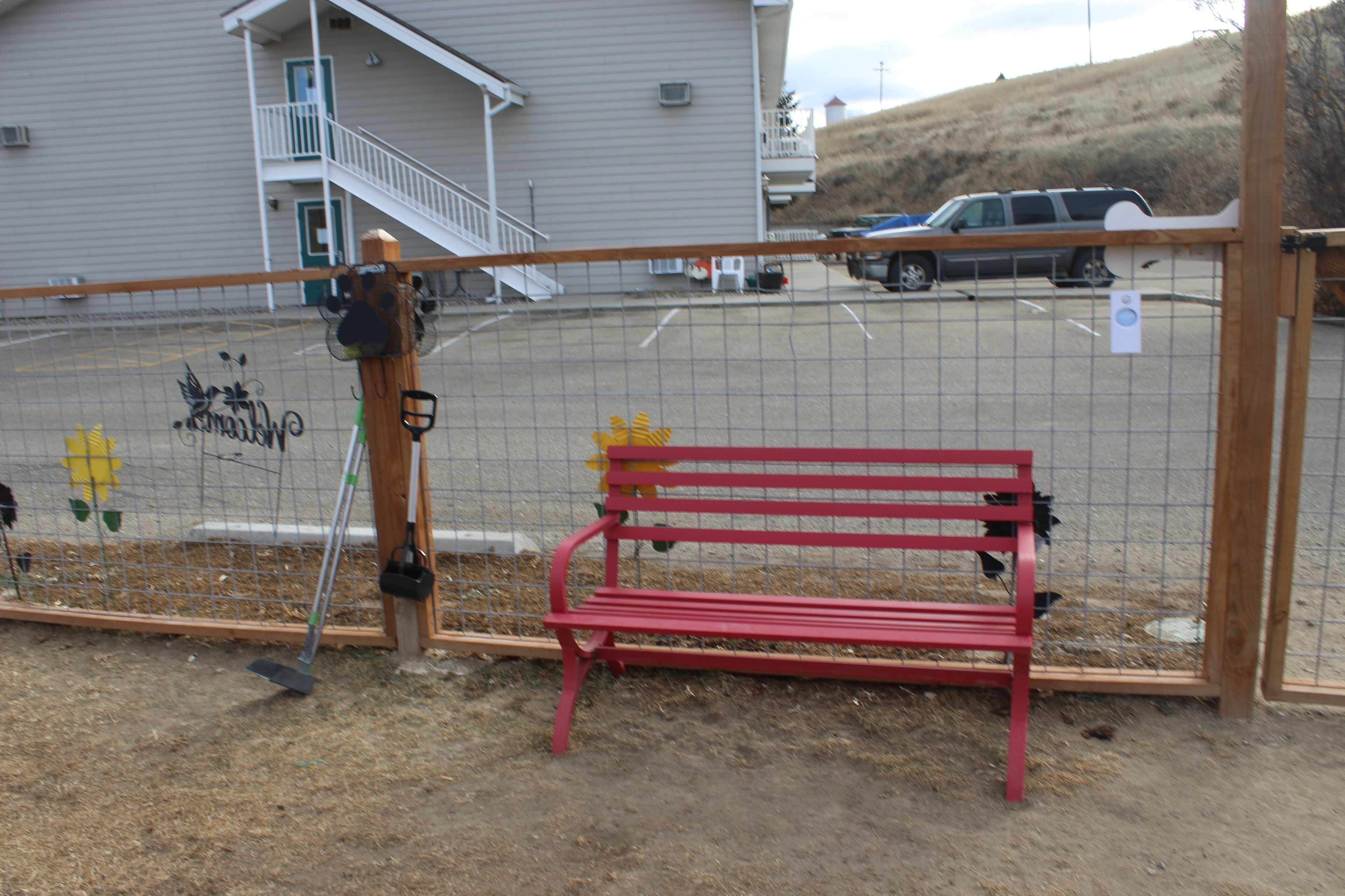 A fenced area with a red bench and a wooden post with a shovel.
