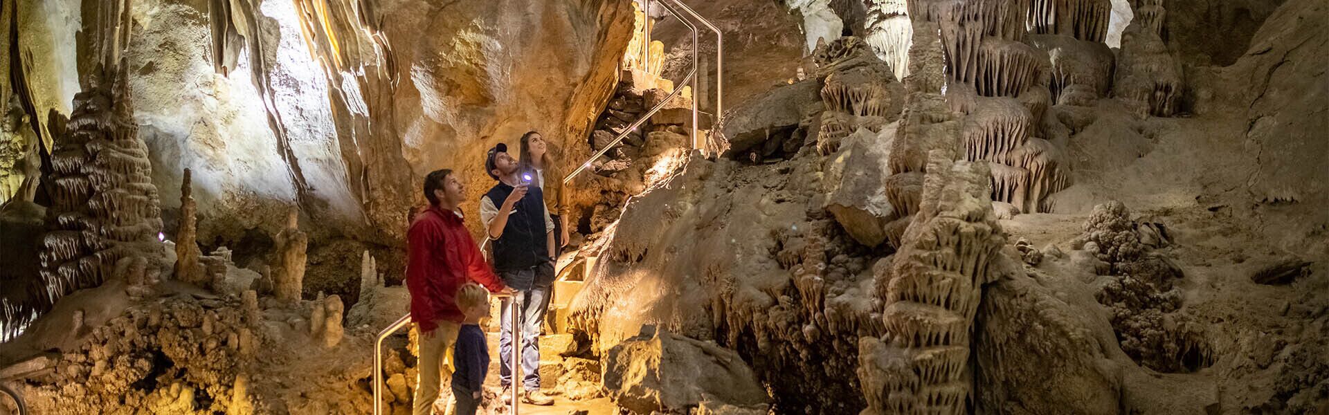 A cave with stalactites and stalagmites, a metal staircase, and visitors exploring.