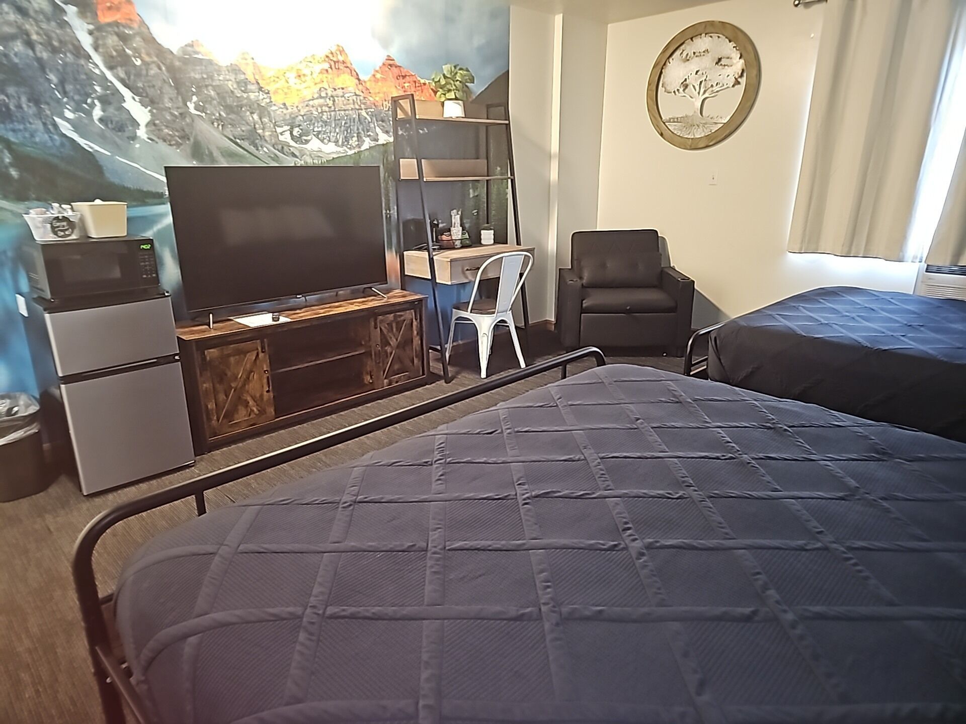 A room with a bed, a desk with a computer, a chair, a TV, and a wall mural.