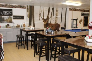 A bar area with a wooden pool table, multiple stools, and a large elk mounted on the wall.