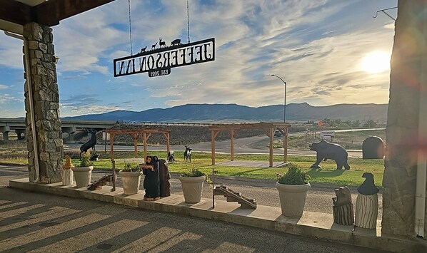A welcome sign, a stone pillar, a covered area with a bench, and a view of mountains in the background.