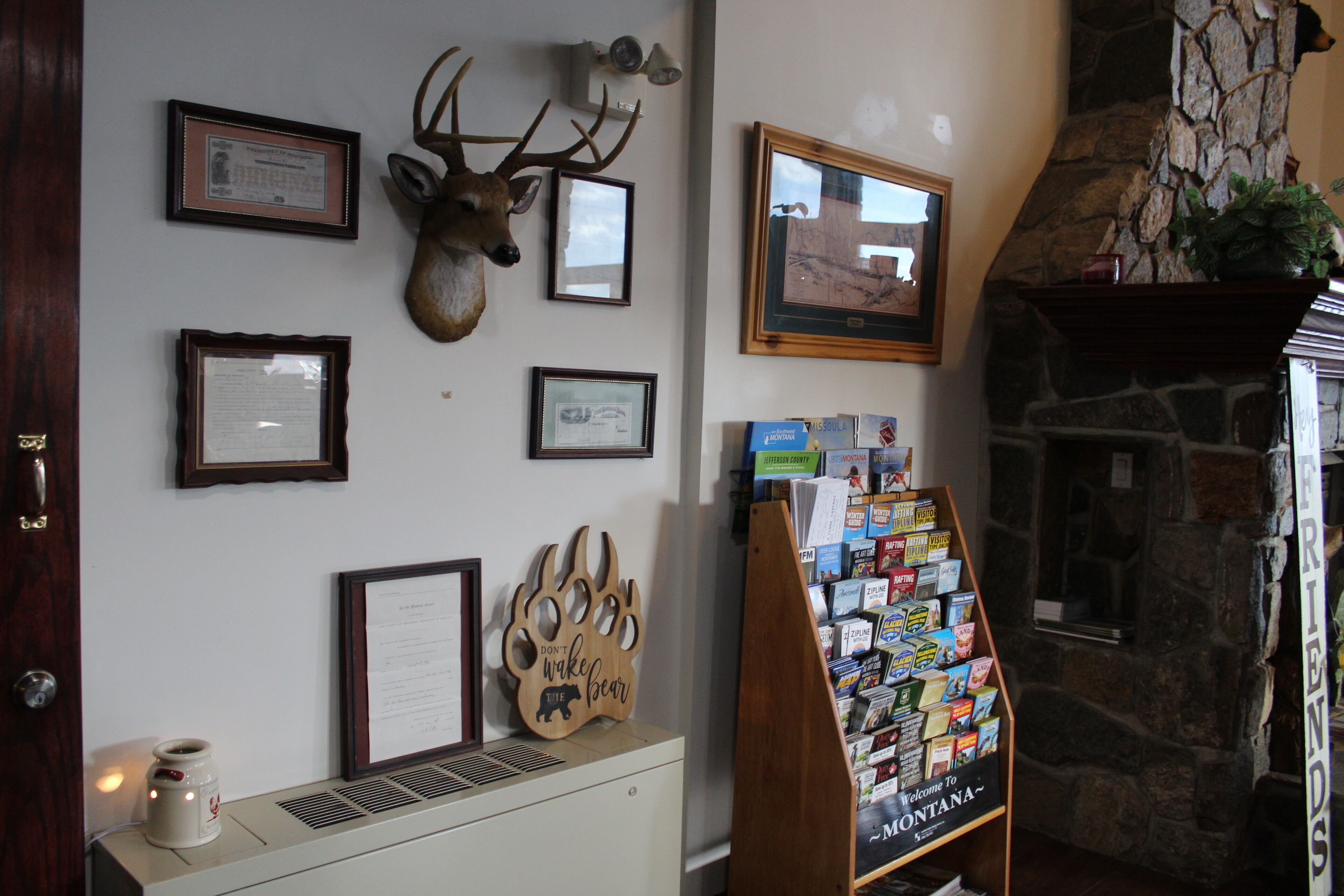 A wall with framed certificates, a mounted deer head, a framed picture, and a welcome sign.