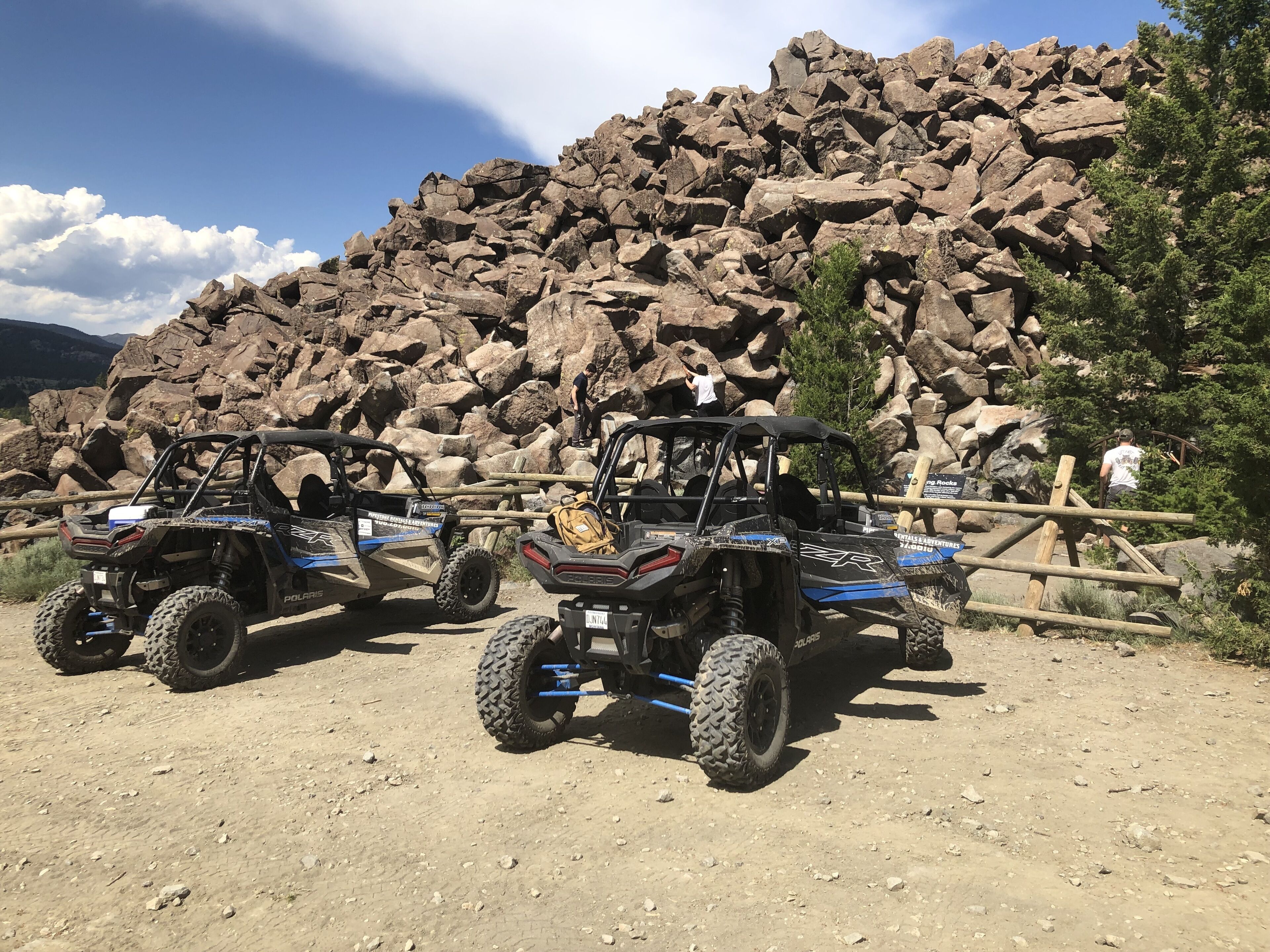 Dos vehículos todo terreno Polaris estacionados en un camino de tierra con montañas rocosas al fondo.