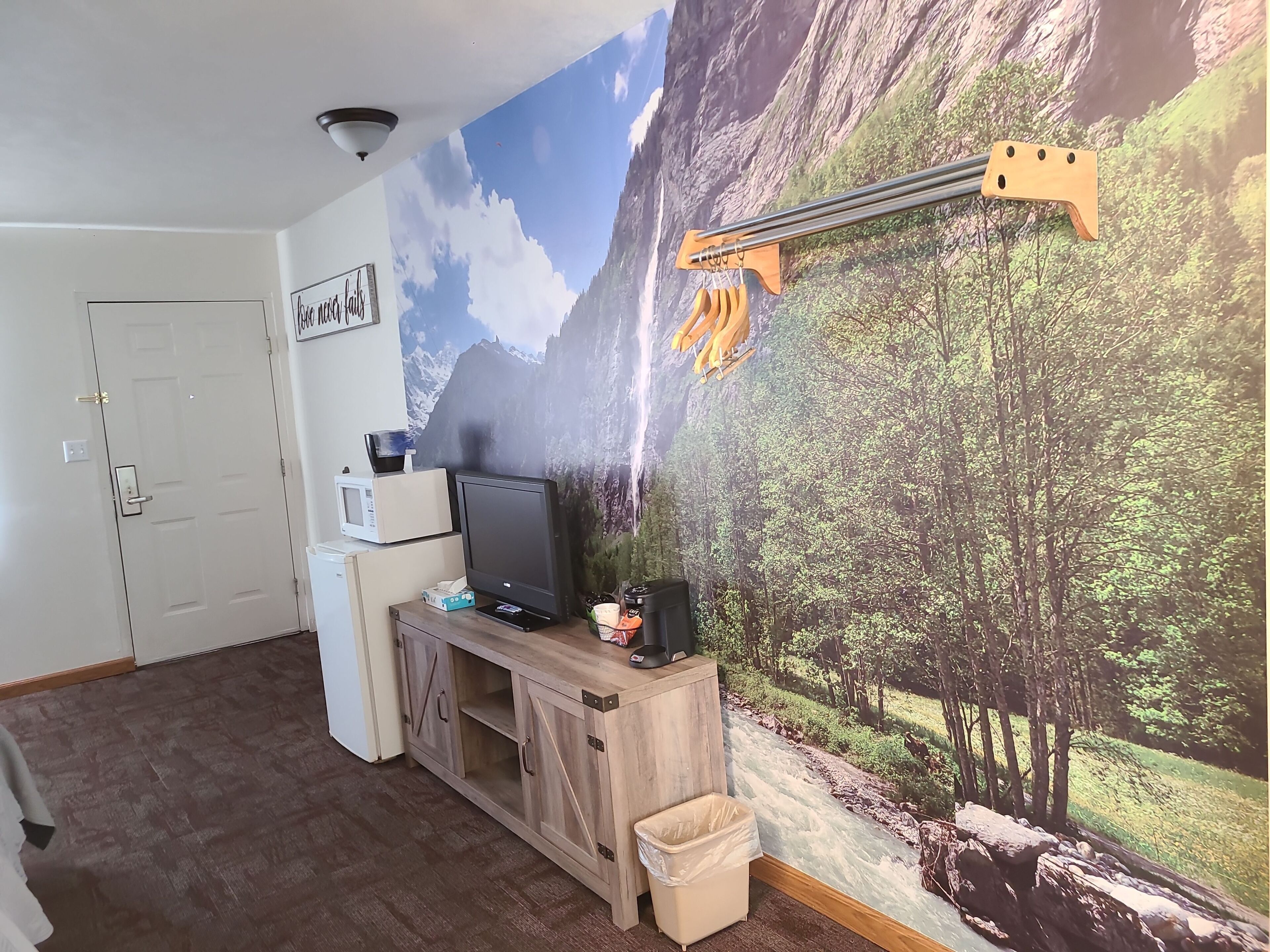 A room with a large mural of a mountain landscape, a wooden desk with a computer, a trash bin, and a door.