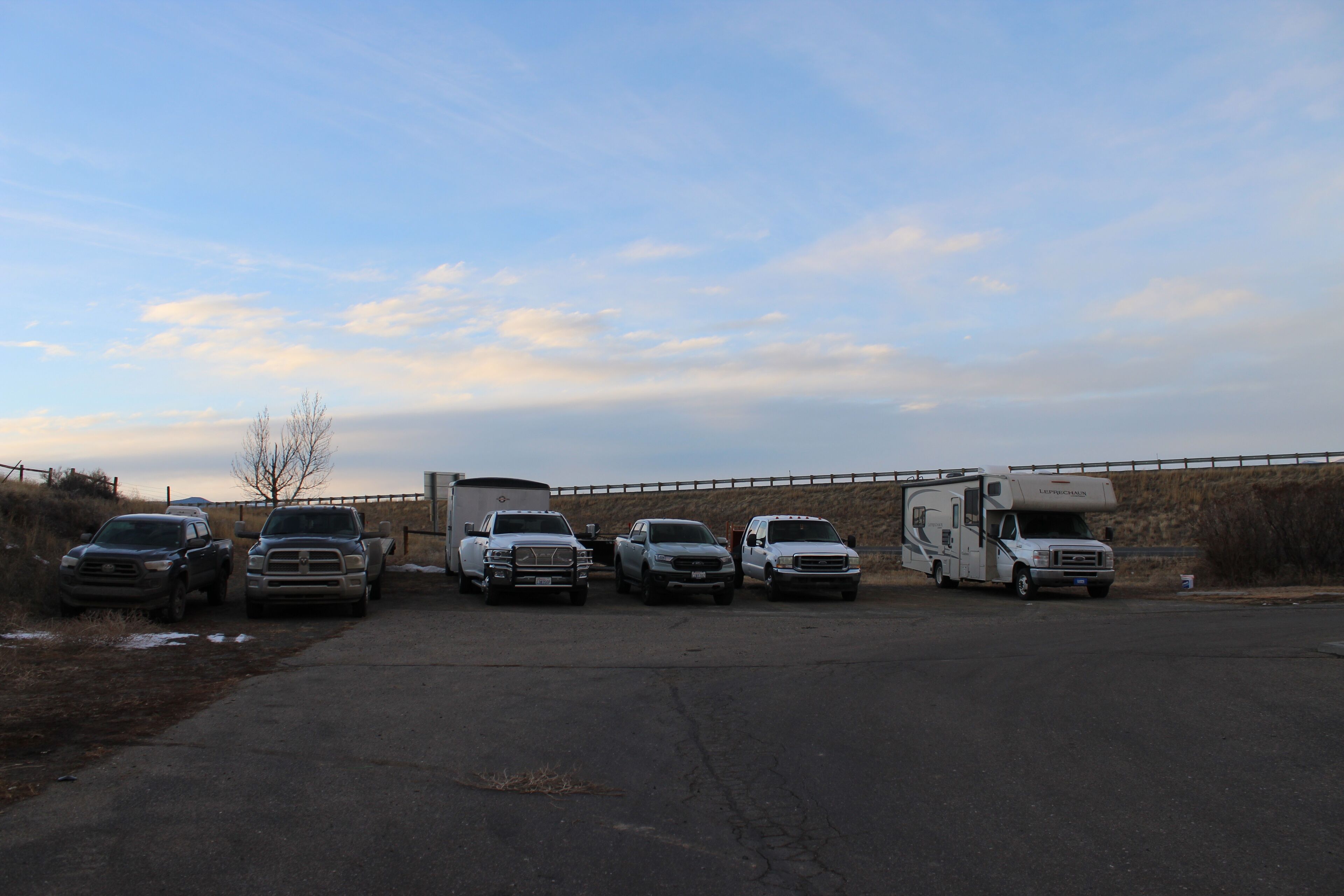 A parking lot with several vehicles, including trucks and a camper, parked in a row.