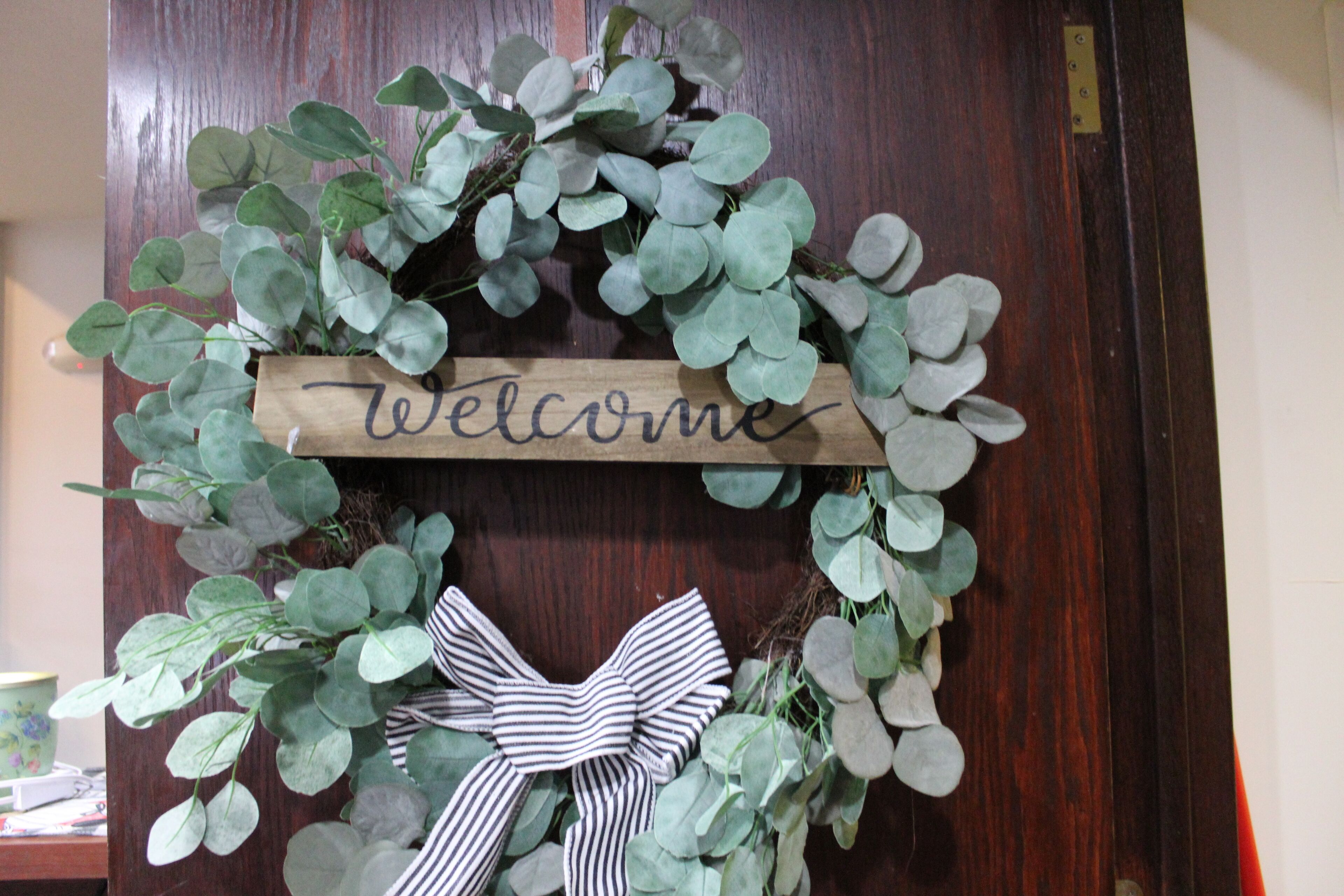 A wooden door with a welcome sign and a decorative bow.