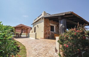 Una villa con fachada de piedra, un porche cubierto y un jardín con plantas en flor.
