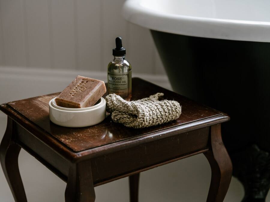 Un petit tabouret en bois, un savon, une bouteille d’huile polyvalente à la rose et une serviette à main tricotée.