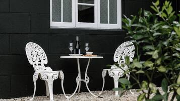 Un espace extérieur aménagé avec des meubles blancs, comprenant deux chaises et une table, placé devant un mur sombre sur lequel se trouve une fenêtre.