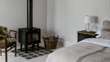 Ein gemütliches Zimmer mit Kamin, einem Korbwägelchen, einem Sessel, einem Nachttisch mit Lampe und einem Bett.