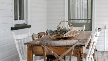 Una mesa de comedor de madera con sillas blancas, una cesta y un farol en una terraza de madera.