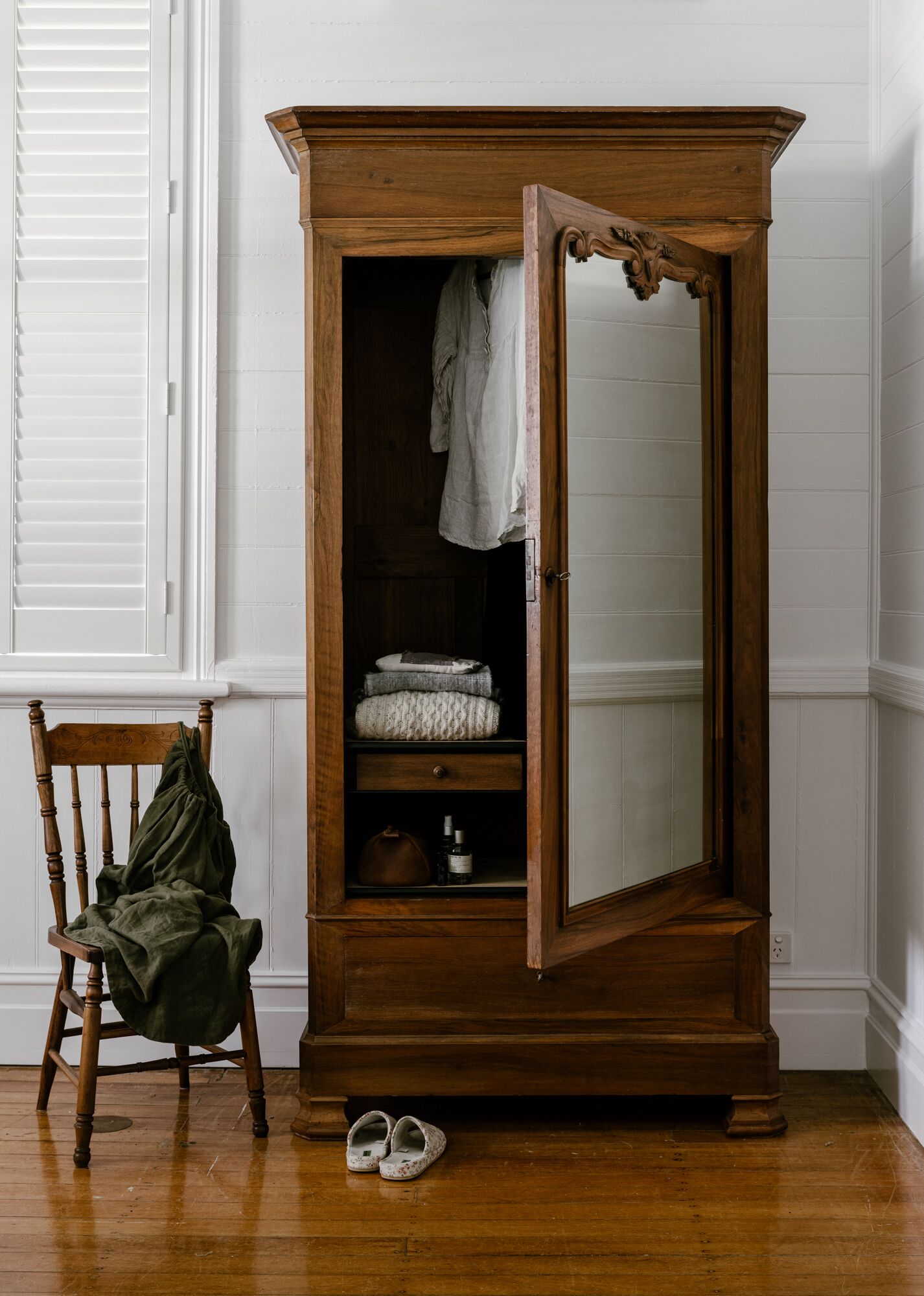 A wooden armoire with a mirror, a chair, and a pair of shoes.