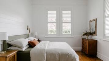 Un dormitorio con cama, mesitas de noche, cómoda, ventana con persianas y espejo.