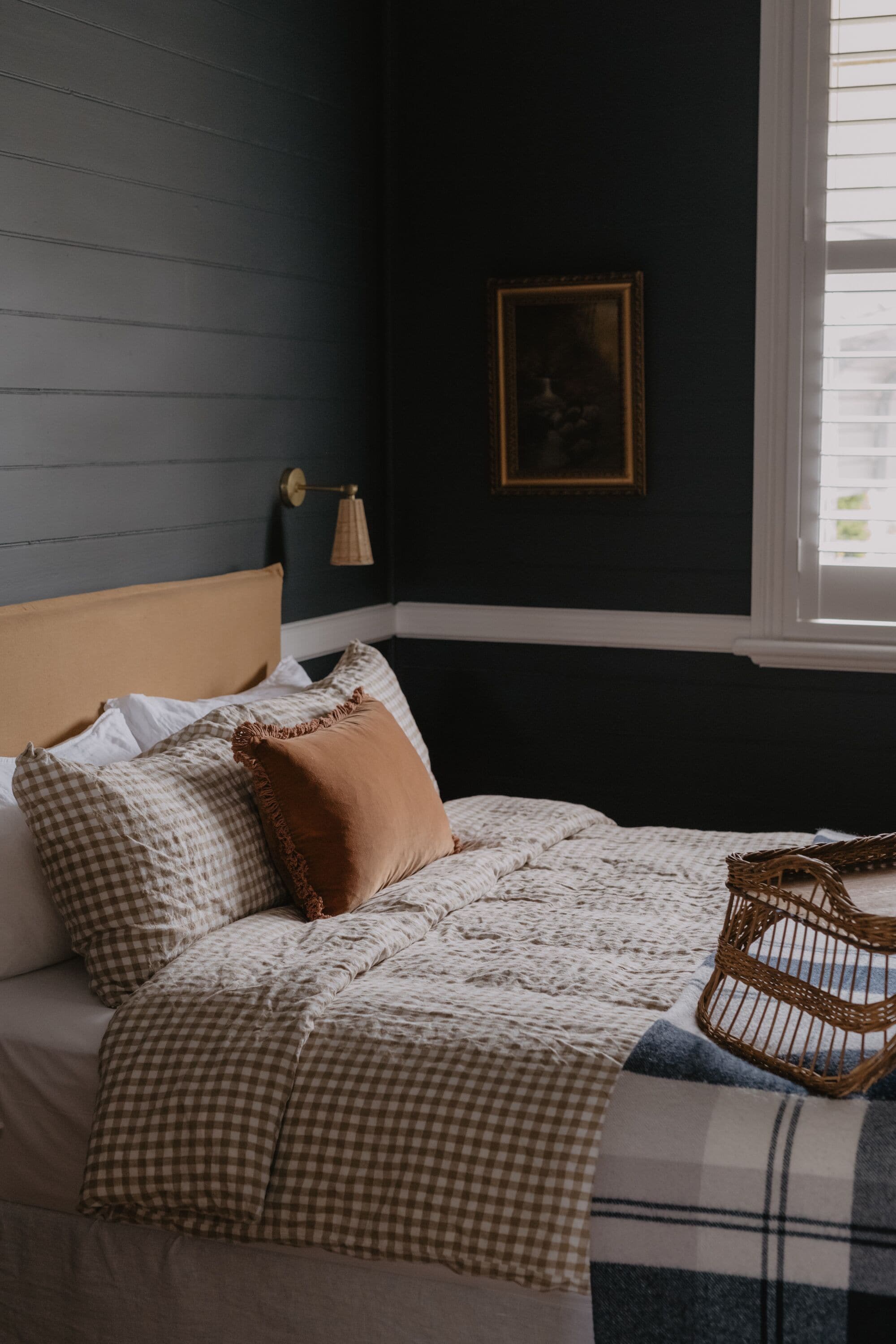 A bed with checkered bedding, a brown pillow, and a woven basket.