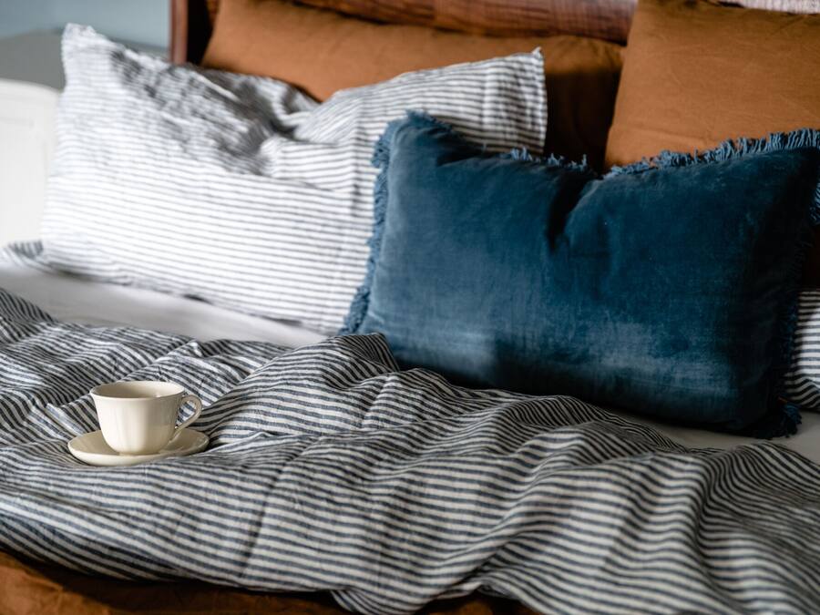 A bed with striped bedding, a dark blue pillow, and a white mug on a saucer.