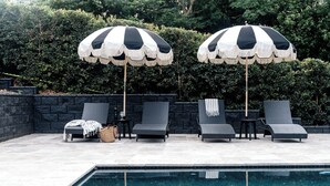 A poolside area with four lounge chairs, two large striped umbrellas, a small table with a bottle and glass, and a woven basket. - Maleny Lodge (Maleny)