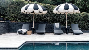 Una piscina al aire libre, sombrillas, sillones reclinables de piscina