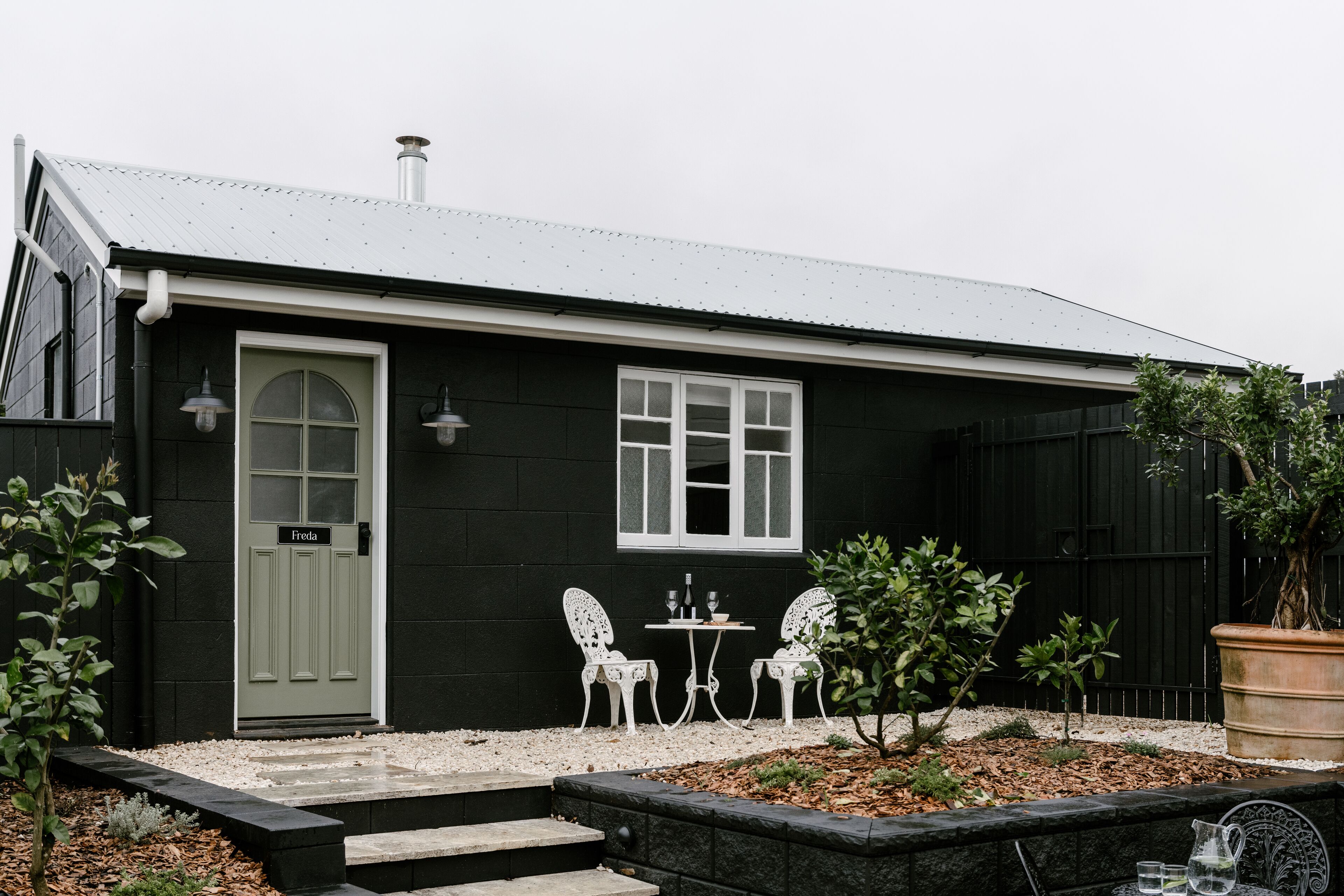 A black house with a green door, two white chairs, and a small table.