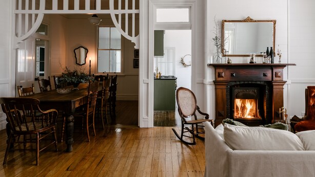 A dining area with a wooden table and chairs, a fireplace with a mirror above, and a cozy seating area with a sofa. - Maleny Lodge (Maleny)