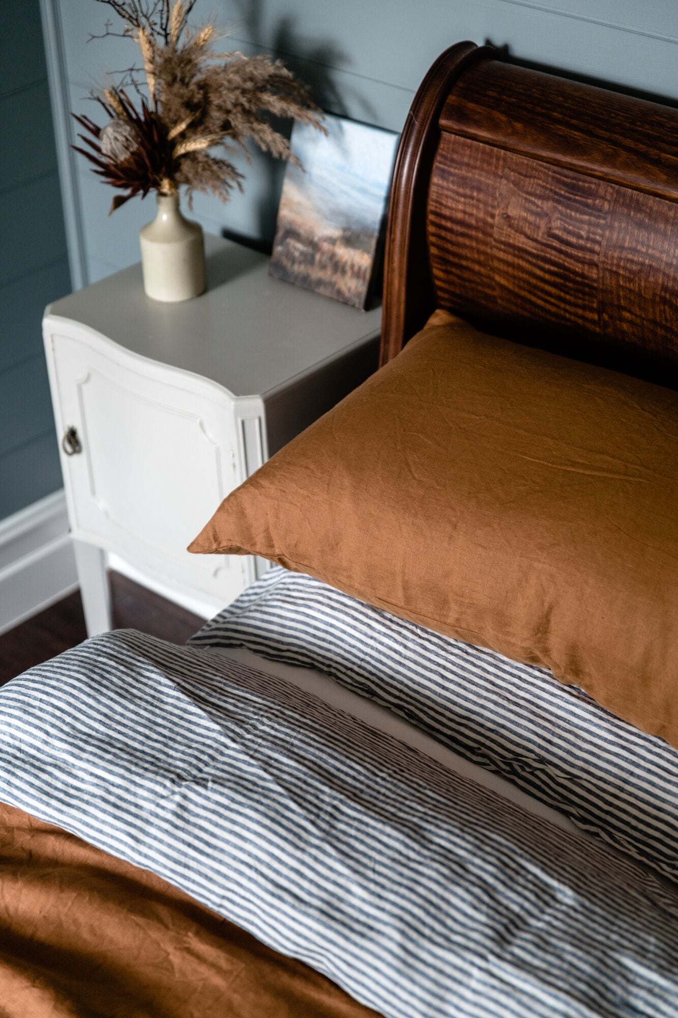 Una cama con ropa de cama a rayas, almohada marrón y cabecera de madera.