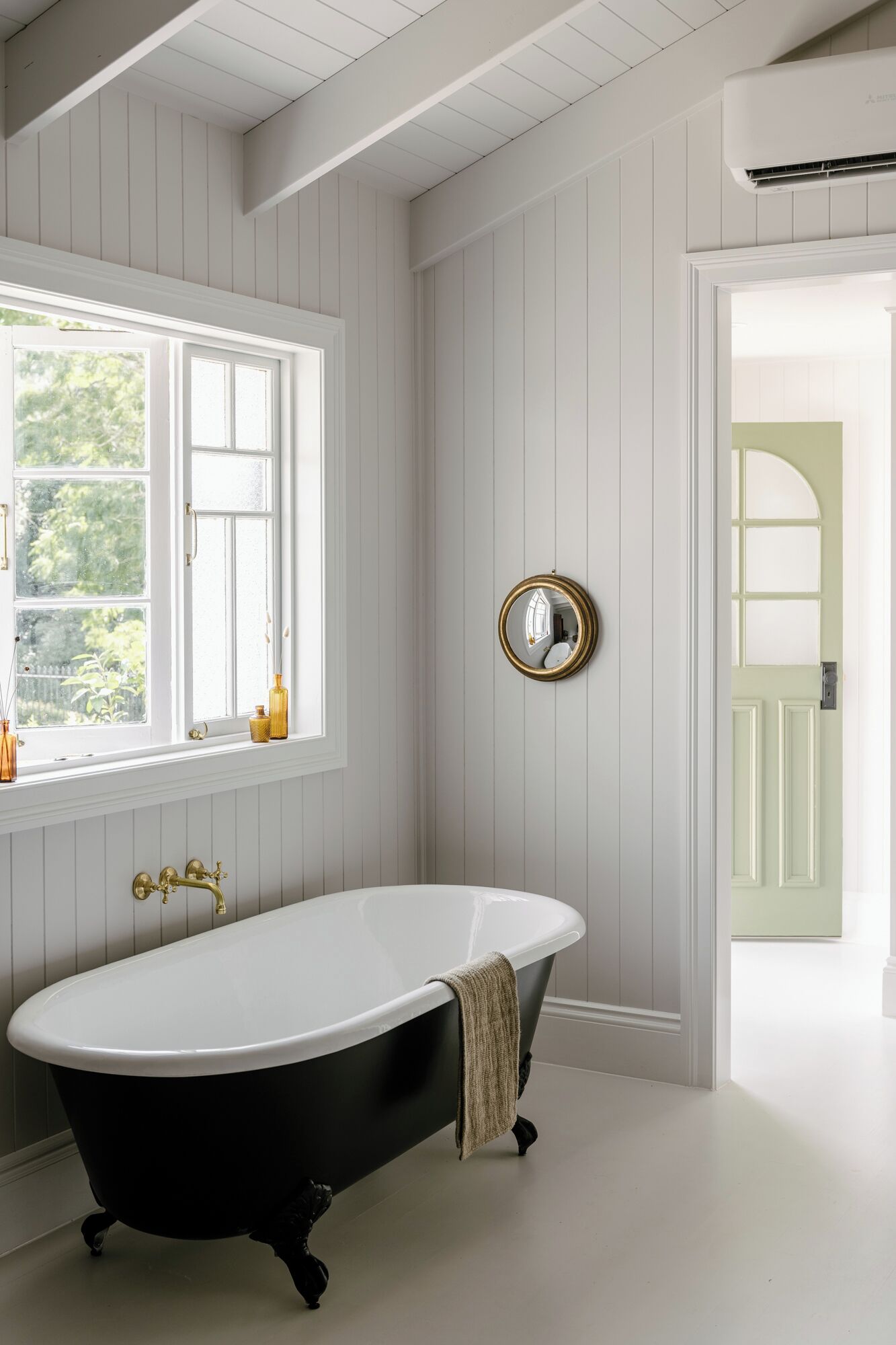 A bathroom with a freestanding bathtub, a window with a view of greenery, and a mirror on the wall.