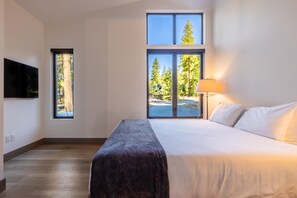 A bedroom with a bed, a TV, a window, and a lamp.