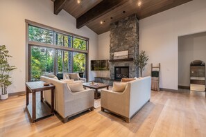 A spacious living room with a stone fireplace, large windows, and a high ceiling.