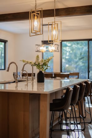 A modern kitchen with a large island, bar stools, pendant lighting, and a view of the outdoors.