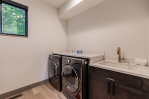 A laundry room with two front-loading washers, a sink, and a window with a view of trees. - Family Friendly w/ Suncadia Pool Access (Cle Elum)