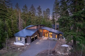 A modern two-story house with a stone exterior, a metal roof, and a driveway leading to a wooden garage.