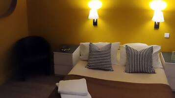 Habitación de hotel con cama, dos lámparas de pared, una planta colgante y un accesorio de iluminación en el techo.