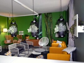 Una sala de estar moderna con paredes verdes, sofá amarillo, sillas blancas y faroles negros colgantes.