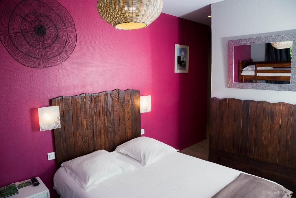 Un dormitorio con cabecera de madera, cama con ropa de cama blanca, espejo montado en la pared y lámpara colgante.