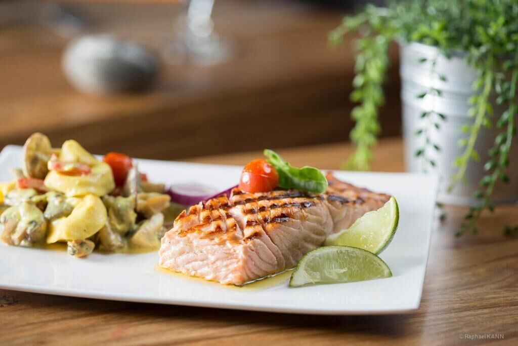 A plate with grilled salmon, a side salad, and lime wedges.