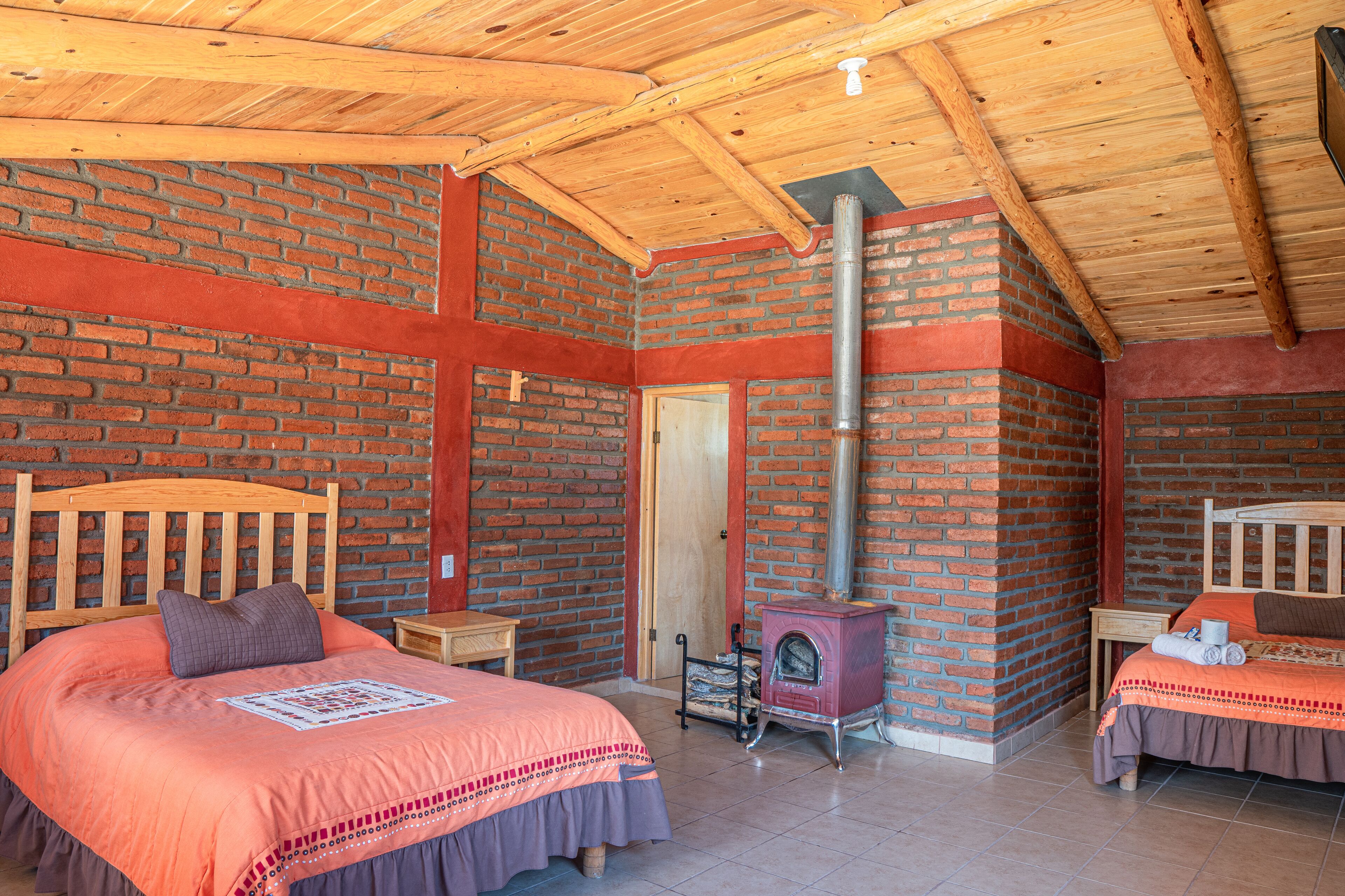 A cozy room with a brick wall, a wooden ceiling, a bed with a headboard, a small table, and a fireplace.