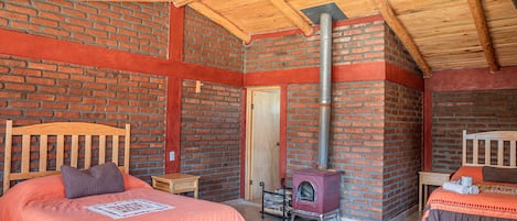 A cozy room with a brick wall, a wooden ceiling, a bed with a headboard, a small table, and a fireplace.