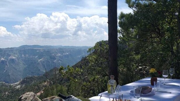 An outdoor dining table set with plates, glasses, and a flower arrangement, overlooking a mountainous landscape. - Cabañas Darely (Urique)