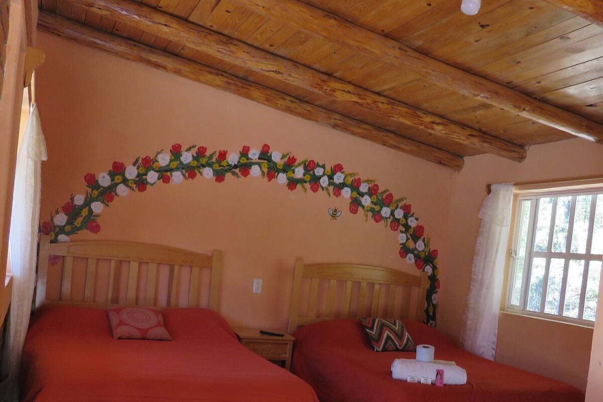 A room with two beds, a wooden table, and a ceiling fan.