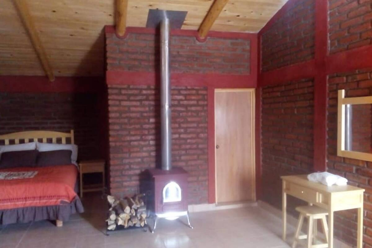 A bedroom with a brick wall, a wooden bed, a wooden table, and a fireplace.