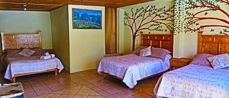 A hotel room with three beds, a wooden ceiling, a painting on the wall, and a tree mural.
