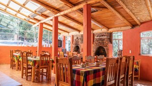 A dining area with wooden tables and chairs, a brick fireplace, and large windows. - Cabañas Darely (Urique)