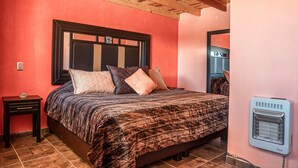 A bedroom with a large bed, a nightstand, a heater, and a wooden ceiling. - Cabañas Darely (Urique)