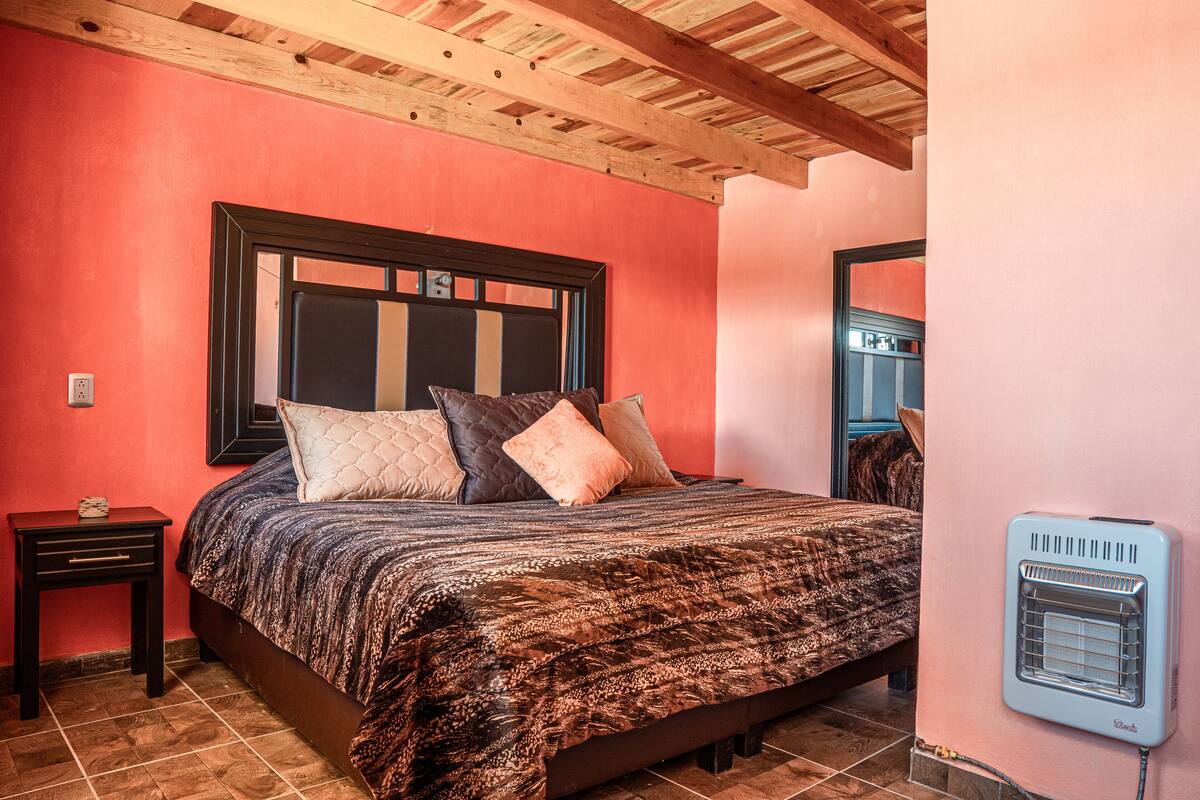 A bedroom with a large bed, a nightstand, a heater, and a wooden ceiling.