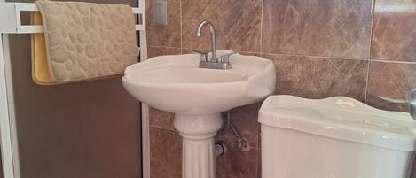 Un baño con lavamanos pedestal, inodoro y toallero.