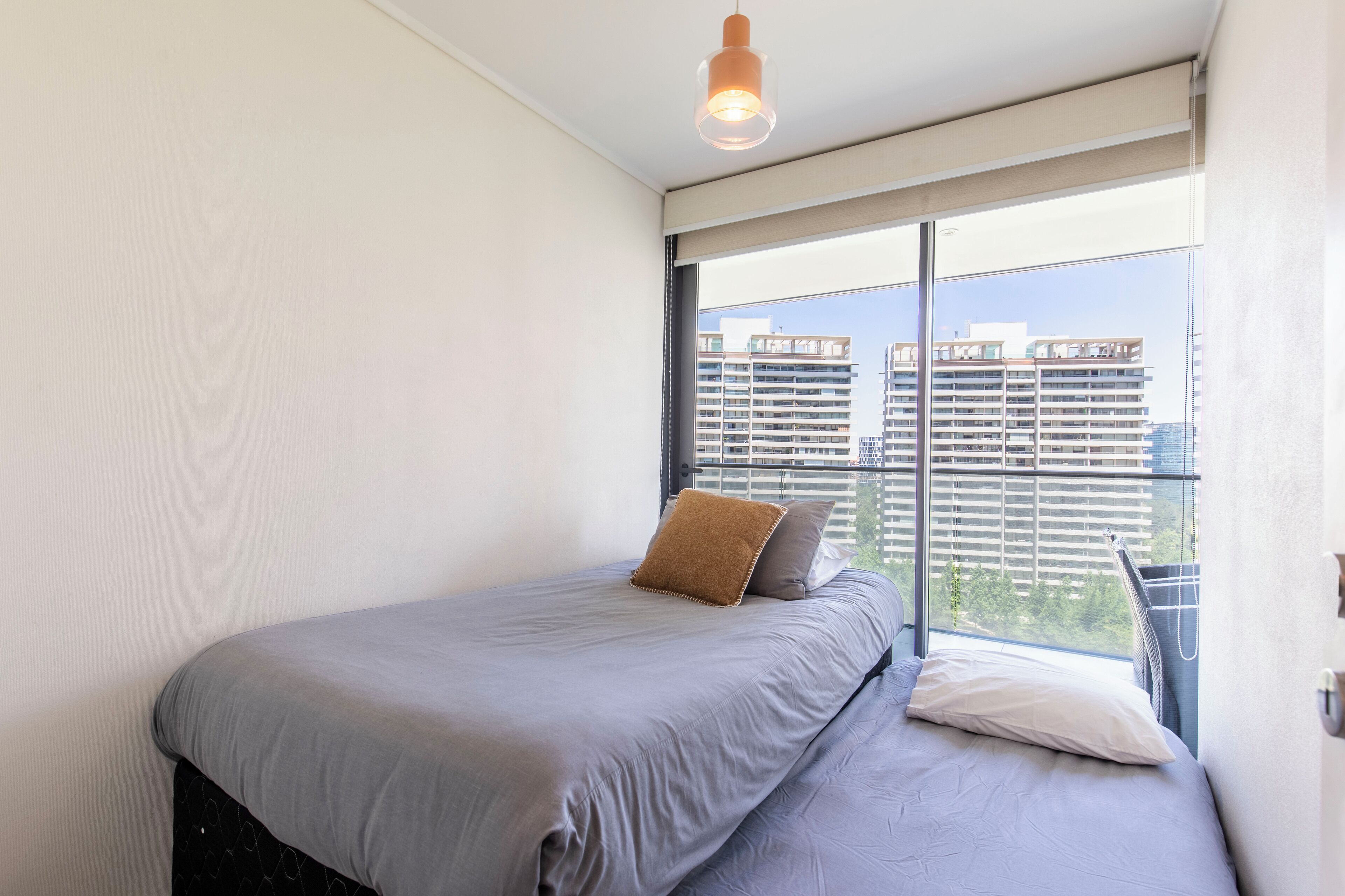 Ein Schlafzimmer mit großem Fenster, einem Bett und einer Pendelleuchte.