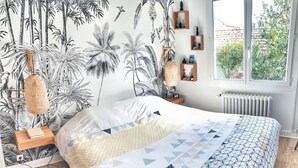 A bedroom with a bed, a nightstand, a lamp, and a window with a view of greenery. - Quiet house + T2, garden & Spa, close to beaches (Anglet)